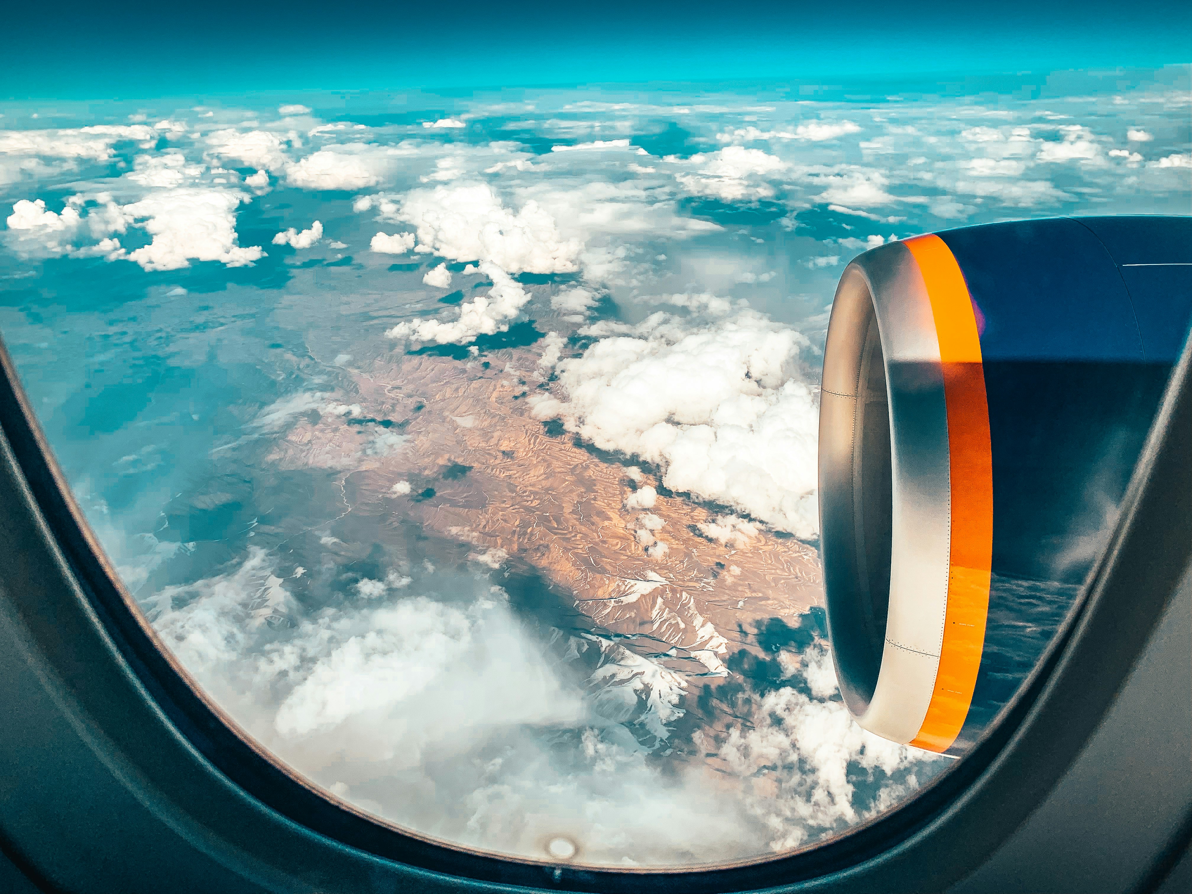Aerial view through an airplane window of a jet engine over clouds and mountains