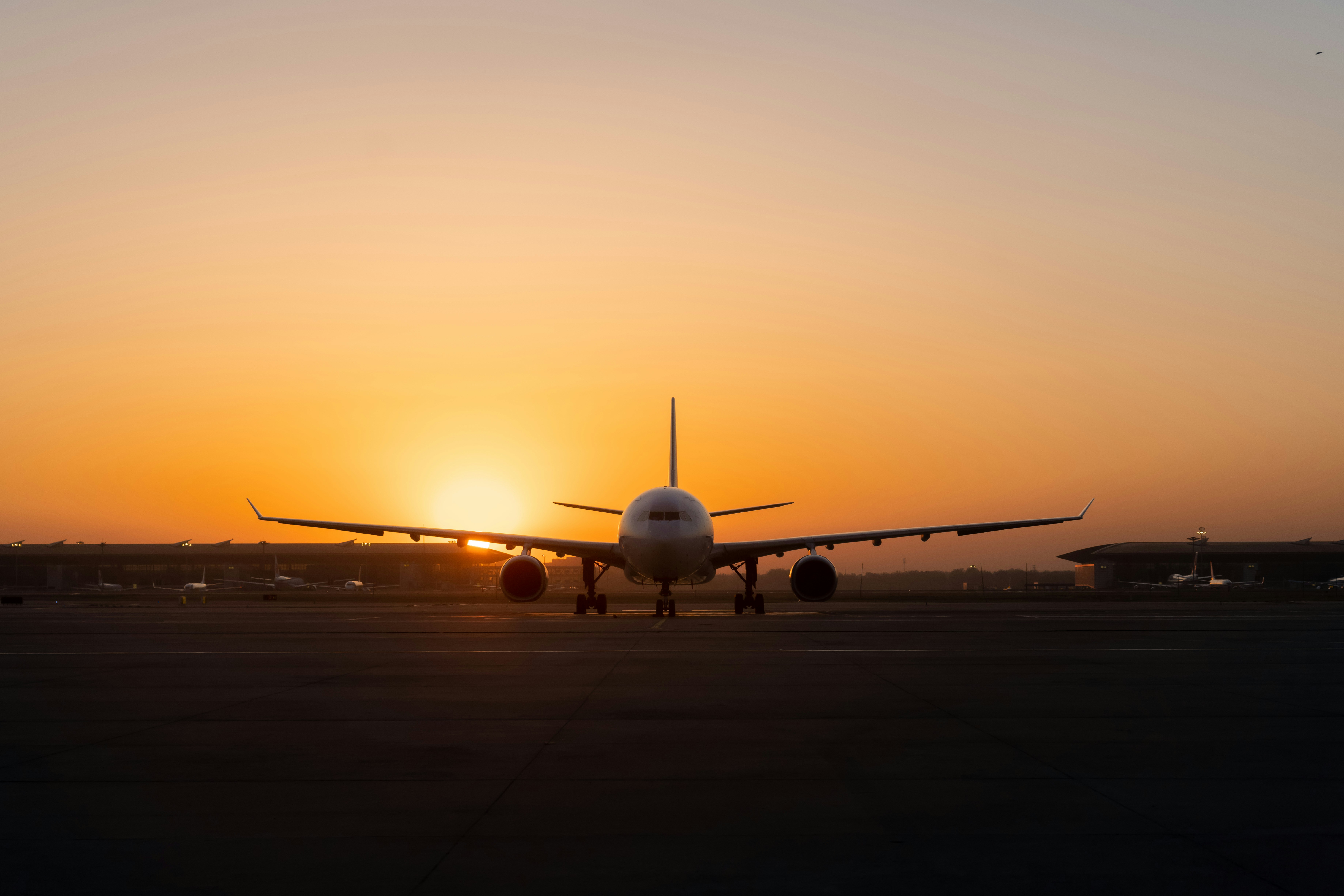 Wide-body cargo jet on an airport tarmac silhouetted against a vivid orange sunset